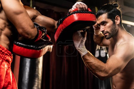 Asiatischer und kaukasischer Muay Thai-Boxer entfesseln in einer heftigen Boxtrainingseinheit oberflächliche Schlagattacken, liefern dem Sparringstrainer Schlagschläge und demonstrieren Muay Thai-Boxtechnik und -Geschick. Impulse
