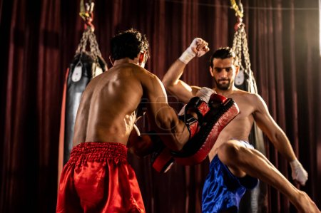 Téléchargez les photos : Le boxeur asiatique et caucasien Muay Thai déclenche une attaque de coups de pied dans une séance d'entraînement de boxe féroce, donnant un coup de pied à l'entraîneur sparring, mettant en valeur la technique et les compétences de boxe Muay Thai. Impulsion - en image libre de droit