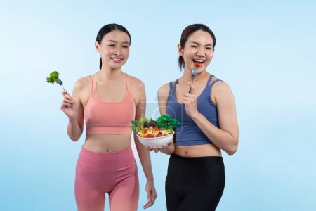 Photo for Two young sporty Asian women in sportswear holding salad bowl fill with fruit and vegetable. Natural youthful and fit body lifestyle people with balance nutrition on isolated background. Vigorous - Royalty Free Image