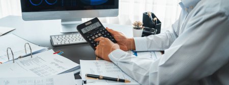 Photo for Corporate auditor calculating budget with calculator on his office desk. Dedicated accountant professional of accounting business company analyzing financial document to forecast income. Insight - Royalty Free Image