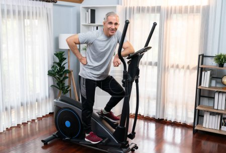 Photo for Active senior man running on elliptical running machine at home portrait as fitness healthy lifestyle and body care after retirement for pensioner. Clout - Royalty Free Image
