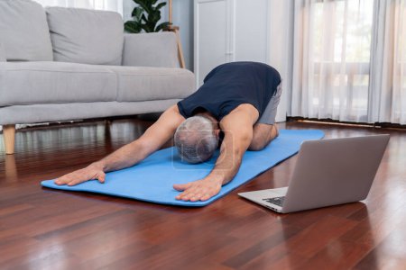 Photo for Senior man in sportswear being doing yoga in meditation posture on exercising mat at home. Healthy senior pensioner lifestyle with peaceful mind and serenity. Clout - Royalty Free Image
