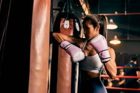 Foto de La boxeadora asiática Muay Thai desencadena un ataque de codo en una feroz sesión de entrenamiento de boxeo, entregando el golpe de codo al equipo de boxeo de la bolsa de patadas, mostrando la técnica y habilidad de boxeo Muay Thai. Impulso - Imagen libre de derechos