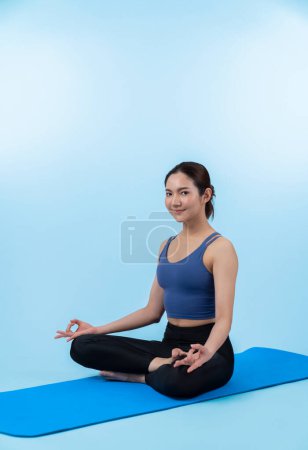 Foto de Mujer asiática en ropa deportiva haciendo ejercicio de yoga en la alfombra de fitness como su rutina de entrenamiento. Cuidado corporal saludable y meditación tranquila en el estilo de vida del yoga en tiro de cuerpo completo sobre fondo aislado. Vigoroso - Imagen libre de derechos