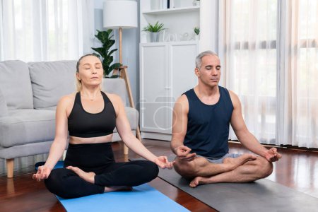 Photo for Happy active senior couple in sportswear being doing yoga in meditation posture on exercising mat at home. Healthy senior pensioner lifestyle with peaceful mind and serenity. Clout - Royalty Free Image