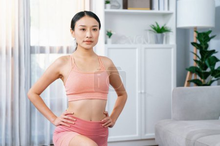 Foto de Joven atractiva mujer asiática en ropa deportiva estiramiento antes de la rutina de ejercicios de fitness. Entrenamiento corporal en casa con una mujer atlética saludable calentándose. Vigoroso - Imagen libre de derechos