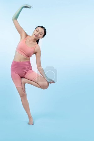 Téléchargez les photos : Femme asiatique en vêtements de sport faisant de l'exercice de yoga en position debout sur la forme physique comme sa routine d'entraînement d'entraînement. Soins du corps sains et mode de vie de yoga de méditation en plan complet sur fond isolé. Vigoureux - en image libre de droit