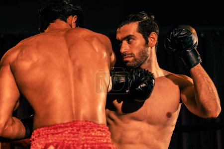 Téléchargez les photos : Le boxeur asiatique et caucasien Muay Thai libère son pouvoir dans un match de boxe féroce. Deux boxeurs MuayThai avec un corps musclé fort échangeant poinçon et frapper avec des prouesses de combat implacables. Impulsion - en image libre de droit