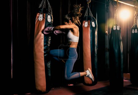 Téléchargez les photos : Femme asiatique Muay boxer thaïlandais avec un corps athlétique et musculaire forte en utilisant son genou et poing coup de pied sac comme son entraînement de boxe dans la salle de gym. Art martial et style de vie sportif. Impulsion - en image libre de droit