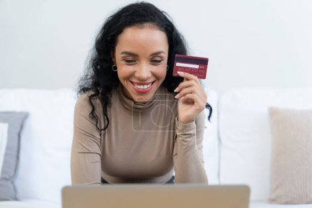 Photo for Young happy woman buy product by online shopping at home while ordering items from the internet with credit card online payment system protected by crucial cyber security from online store platform - Royalty Free Image