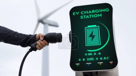 Photo for EV charger from EV car charging station in nature and wind turbine farm reducing CO2 emission. Technological advancement of alternative energy sustainability and EV car. Peruse - Royalty Free Image
