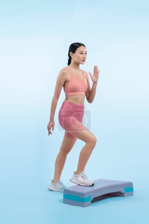 Photo for Vigorous energetic woman doing exercise at on studio short isolated background with cardio aerobic step workout. Young athletic asian woman dexterity and endurance training session concept. - Royalty Free Image