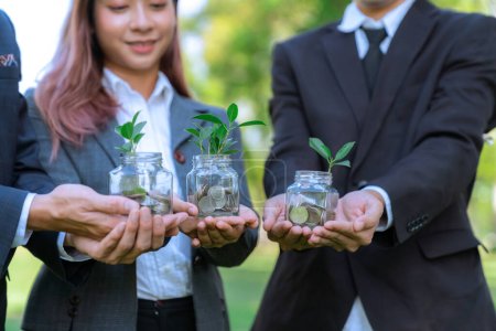 Photo for Concept of sustainable money growth investment with glass jar filled with money savings coins with businesspeople as eco-friendly financial investment nurtured with nature and healthy retirement. Gyre - Royalty Free Image