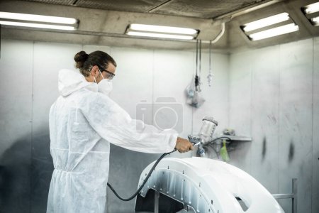 Photo for Automotive service worker in protective gear expertly applying color paint in to cars bodywork with spray gun or respirator painting in chamber workshop. Car paint service for scratch refinish. Oxus - Royalty Free Image