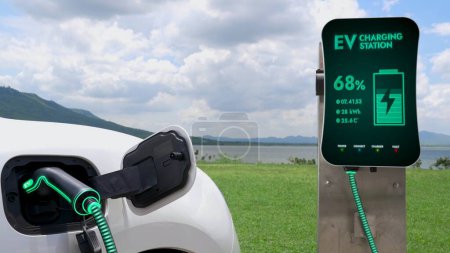 Téléchargez les photos : Voiture électrique branchée avec borne de recharge pour recharger la batterie par câble chargeur EV avec fond nature et lac. Future voiture innovante ev et la durabilité énergétique. Pertinence - en image libre de droit