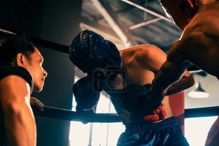 Photo for Boxer fighter competitor struggle with pain and disadvantage on boxing match at the ring while referee closely observe action. Boxer with safety helmet try to defense himself. Impetus - Royalty Free Image
