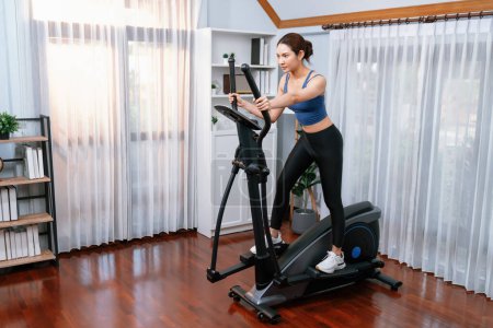 Energetic and strong athletic asian woman running on elliptical running machine at home. Pursuit of fit physique and commitment to healthy lifestyle with home workout and training. Vigorous