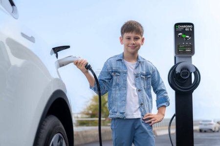 Photo for Little boy recharging eco-friendly electric car from EV charging station. EV car road trip travel by the seashore by alternative vehicle powered by clean renewable and sustainable energy. Perpetual - Royalty Free Image