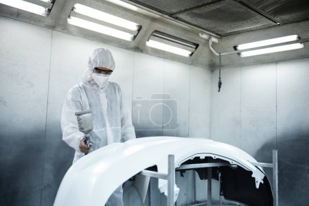 Photo for Automotive service worker in full protective gear expertly apply color paint in to cars bodywork with spray gun or respirator painting in chamber workshop. Car paint service for scratch refinish.Oxus - Royalty Free Image
