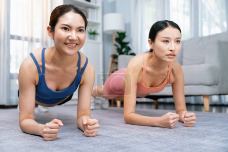 Foto de Ajuste joven mujer asiática cepillando en el piso de la sala de estar con su entrenador o compañero de ejercicio. Rutina de entrenamiento de estilo de vida saludable en casa. Equilibrio y resistencia ejerciendo el concepto. Vigoroso - Imagen libre de derechos