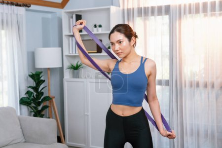 Photo for Vigorous energetic woman doing exercise at home, stretching resistance sport band for muscle gain. Young athletic asian woman strength and endurance training session as home workout routine concept. - Royalty Free Image