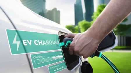 Photo for Hand insert EV charger and recharge electric car from charging station displaying futuristic battery status hologram on ESG green city park background. Smart sustainable clean energy. Peruse - Royalty Free Image