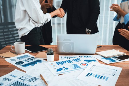 Photo for Focus financial data dashboard paper by business intelligence display graph, chart and statistic report on office table with blurred business people shake hand in corporate background. Habiliment - Royalty Free Image
