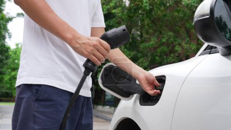Photo for Progressive man install power cable plug to his electric vehicle, EV car from home charging station. Electric car driven by clean and renewable energy to preserve environment. Eco-friendly automobile. - Royalty Free Image