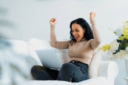 Téléchargez les photos : Femme d'affaires afro-américaine réussie se sentent heureux au travail crucial sur ordinateur portable tout en étant assis sur le canapé à la maison - en image libre de droit