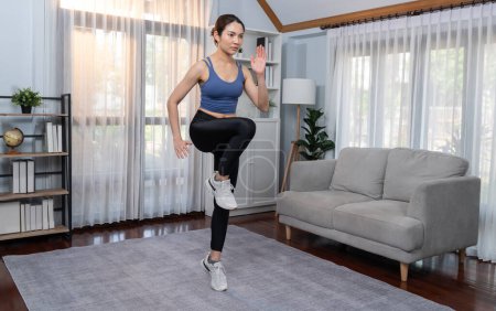 Photo for Energetic and strong athletic asian woman running in place at her home. Pursuit of fit physique and commitment to healthy lifestyle with home workout and training. Vigorous - Royalty Free Image
