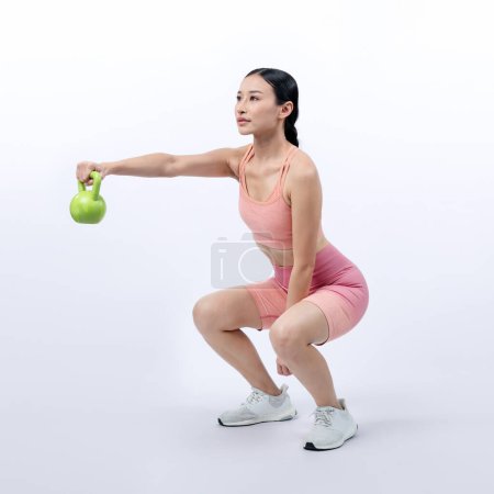 Photo for Vigorous energetic woman doing kettlebell weight lifting exercise on isolated background. Young athletic asian woman strength and endurance training session as body workout routine. - Royalty Free Image