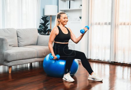 Photo for Athletic and sporty senior woman sitting on fit ball while engaging in weight lifting with dumbbell at home exercise as concept of healthy fit body lifestyle after retirement. Clout - Royalty Free Image