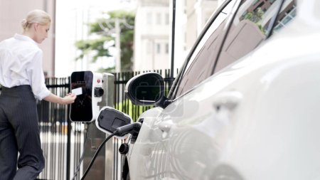 Photo for Progressive businesswoman install charger plug from charging station to his electric car before driving around city center. Eco friendly rechargeable car powered by sustainable and clean energy. - Royalty Free Image