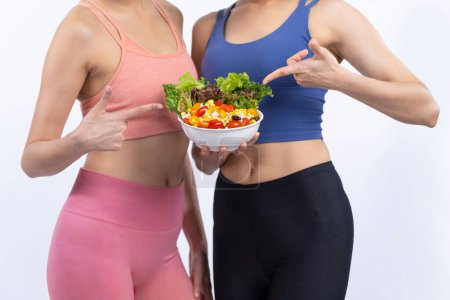 Foto de Dos jóvenes mujeres asiáticas deportivas en ropa deportiva sosteniendo ensaladera llenan con frutas y verduras. Natural joven y en forma de personas de estilo de vida corporal con nutrición de equilibrio en un fondo aislado. Vigoroso - Imagen libre de derechos