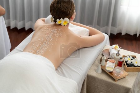 Photo for Woman customer having exfoliation treatment in luxury spa salon with warmth candle light ambient. Salt scrub beauty treatment in health spa body scrub. Quiescent - Royalty Free Image