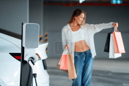 Photo for Young woman travel with EV electric car to shopping center parking lot charging in downtown city showing urban sustainability lifestyle by green clean rechargeable energy of electric vehicle innards - Royalty Free Image