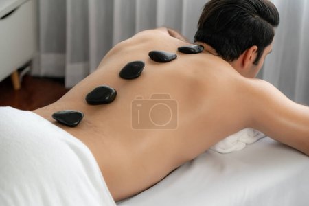 Photo for Hot stone massage at spa salon in luxury resort with day light serenity ambient, blissful man customer enjoying spa basalt stone massage glide over body with soothing warmth. Quiescent - Royalty Free Image