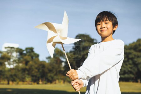 Foto de Pequeño niño asiático sosteniendo molino de viento o modelo de maqueta de turbina eólica para promover la utilización de tecnología de energía limpia y renovable ecológica para la generación futura y la Tierra sostenible. Gyre. - Imagen libre de derechos