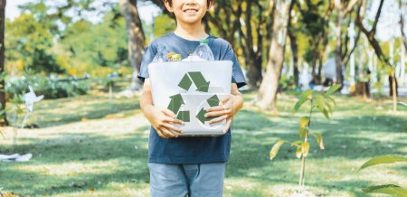 Téléchargez les photos : Joyeux jeune garçon asiatique tenant la corbeille symbole de recyclage sur le parc naturel vert de la lumière du jour promouvoir le recyclage des déchets, réduire et réutiliser les encouragements pour une sensibilisation éco durable pour les générations futures. Pneumatique - en image libre de droit