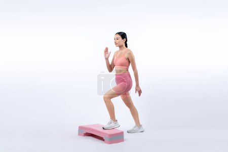 Photo for Vigorous energetic woman doing exercise at on studio short isolated background with cardio aerobic step workout. Young athletic asian woman dexterity and endurance training session concept. - Royalty Free Image