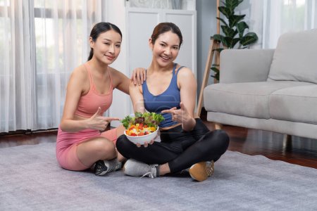 Photo for Young sporty Asian women in sportswear holding salad bowl together fill with vibrant of fruit and vegetable. Natural youthful and fit body lifestyle with balance nutrition and home exercise. Vigorous - Royalty Free Image
