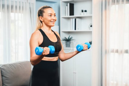 Photo for Athletic and sporty senior woman engaging in body workout routine with lifting dumbbell at home as concept of healthy fit body with body weight lifestyle after retirement. Clout - Royalty Free Image