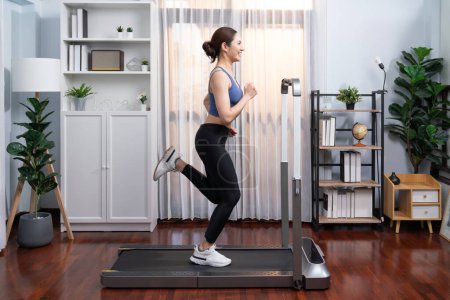 Photo for Full length side view of energetic and strong athletic asian woman running running machine at home. Pursuit of fit physique and commitment to healthy lifestyle with home workout and training. Vigorous - Royalty Free Image