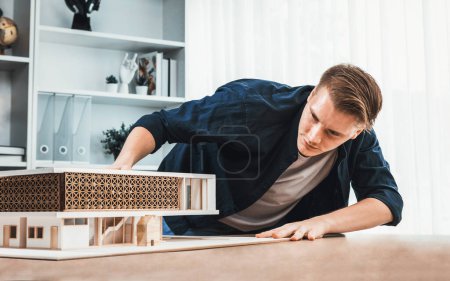 Foto de Arquitecto diseñador estudia elegante modelo de casa, revisando el diseño de la estructura para la mejora con el plan de construcción en la mesa. Creatividad e innovación en el diseño arquitectónico. Iteración - Imagen libre de derechos