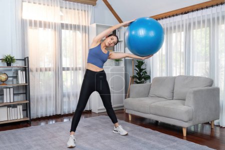 Photo for Young attractive asian woman in sportswear hold and lift fit ball targeting on abs muscle for effective energetic home exercise routine. Vigorous - Royalty Free Image