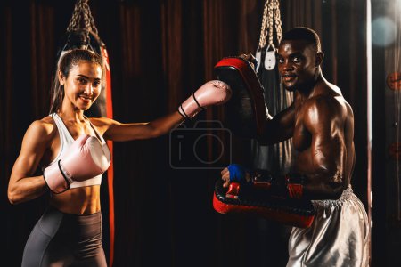 Foto de Mujer asiática muay tailandesa boxeadora con musculoso y fuerte entrenamiento físico con su entrenador personal o entrenador en el gimnasio con guantes y manoplas de puñetazos. Arte marcial y concepto deportivo. Impulso - Imagen libre de derechos