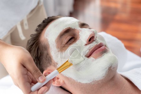 Photo for Serene ambiance of spa salon, man customer indulges in rejuvenating with luxurious face cream massage with modern daylight. Facial skin treatment and beauty care concept. Quiescent - Royalty Free Image