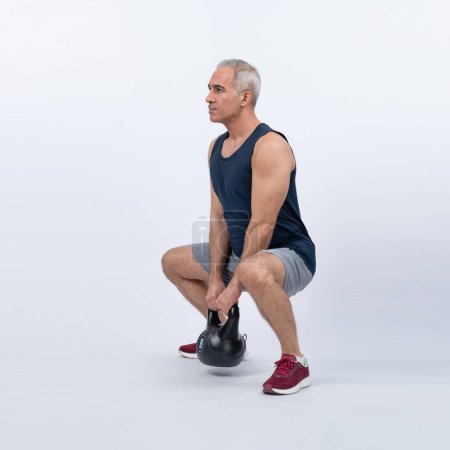 Photo for Full body length shot athletic and sporty senior man doing squat with kettlebell for body workout on isolated background. Healthy active physique and body care lifestyle after retirement. Clout - Royalty Free Image