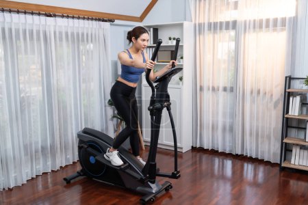 Photo for Energetic and strong athletic asian woman running on elliptical running machine at home. Pursuit of fit physique and commitment to healthy lifestyle with home workout and training. Vigorous - Royalty Free Image