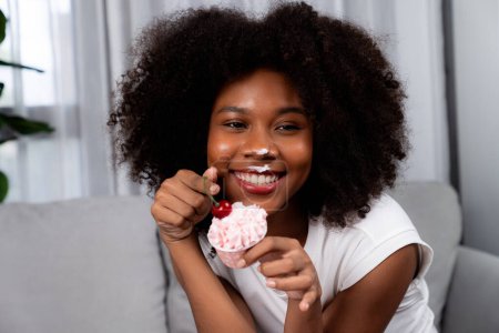 Photo for Funny beautiful young African blogger on mess face presenting cupcake in concept special cuisine. Content creating of social media online with favorite tasty sweets bakery dish. Tastemaker. - Royalty Free Image